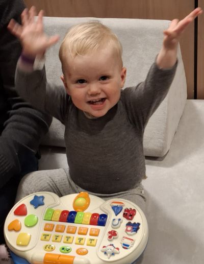 A smiling toddler with both arms in the air, playing with a toy keyboard