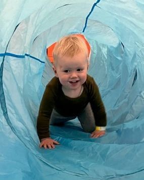 A smiling toddler crawling through a blue play tunnel